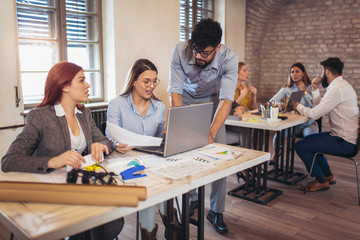 Wall Mural - Group of young business people in smart casual wear working together in creative office using laptop.