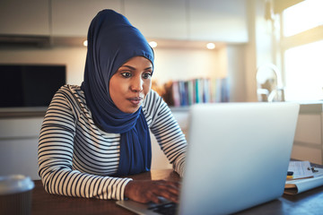 Wall Mural - Young Arabic woman working on a laptop in her kitchen