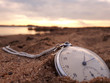 Old pocket watch in the sand during sunset