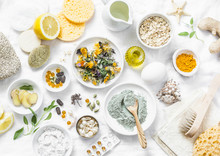 Home Beauty Products - Clay, Oatmeal, Coconut Oil, Turmeric, Lemon, Scrub, Dry Flowers And Herbs, Sponges, Soap, Facial Brush On Light Background, Top View. Skin Youthfulness, Beauty Concept. Flat Lay