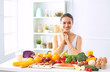 © lenetsnikolai - happy young housewife sitting in the kitchen preparing food from a pile of diverse fresh organic fruits and vegetables