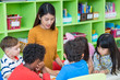 © weedezign - Asian female teacher teaching mixed race kids reading book in classroom,Kindergarten pre school concept.