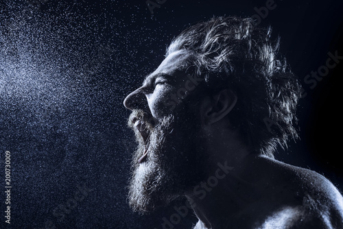 Fotomural A bearded man angrily screams into a spray of water against a black background