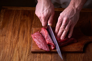 Wall Mural - Strong professional man's hands cutting raw beefsteak, selective focus, close-up