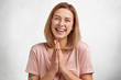 © wayhome.studio  - Studio shot of beautiful smiling female keeps palm together, has joyful expression, asks husband to buy her new outfit, being in good mood, isolated over white studio background. Pleading woman