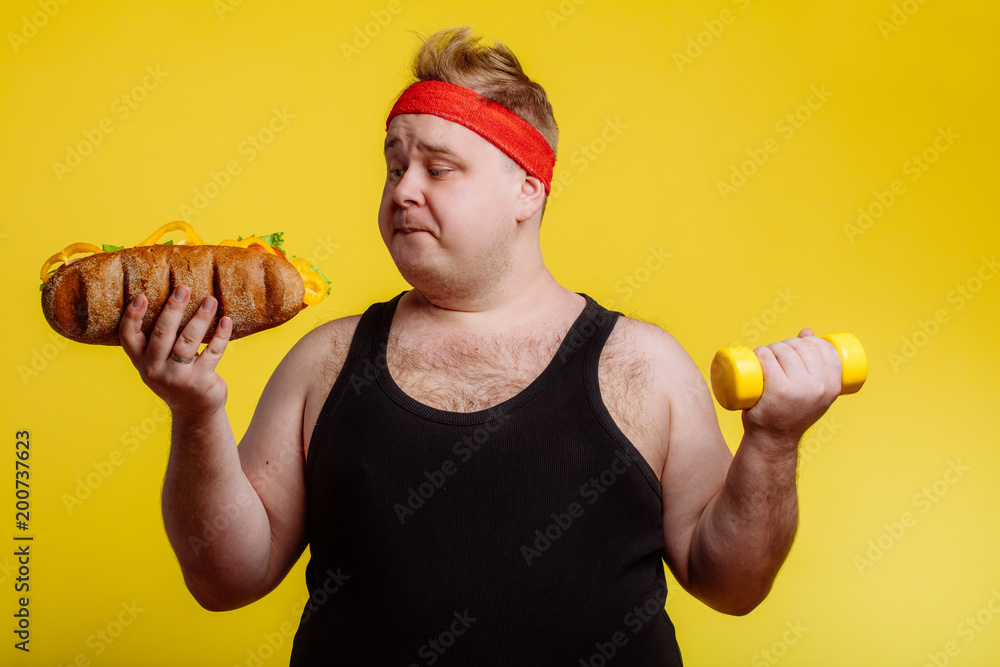 Fat sportsman has ruined the diet with yummy humburger. Gluttony. - obrazy, fototapety, plakaty 