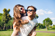 © Look! - Pretty girl with long curly hair is riding on back of handsome guy in park. They wear sunglasses and have fun.
