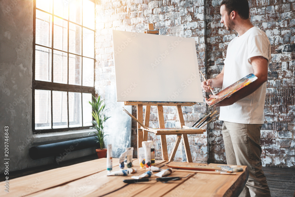 Man artist stands in front of a blank canvas on easel with palette in ...
