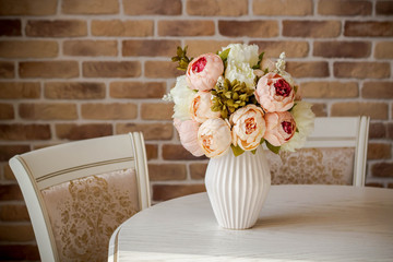 Decoration artificial peonies flower in the vase on the white table with brick background.