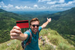 © RealPeopleStudio - Young smiling male showing empty credit card. He is standing on top of mountain and showing the outdoor beauty.