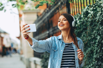 Wall Mural - Young woman listens to music via headphones and smartphone in the city