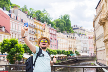 Wall Mural - Handsome man taking selfie with mobile smart phone camera in european city. Vacation, travel and holiday concept.