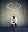 Sad business man sitting on a chair looking down with a rain cloud above him