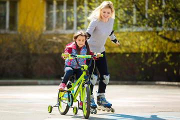 A young mother roller skating. Daughter riding a bicycle