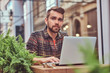 © Fxquadro - Portrait of a smiling fashionable bearded male with a stylish haircut, dressed in a flannel shirt, sitting in a cafe outdoors.