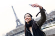 © nenetus - Pretty asian young woman taking a selfie in front of Eiffel tower in Paris while listening to music.
