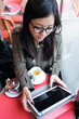 © nenetus - Beautiful young asian woman using her digital tablet while drinking coffee in coffee shop.