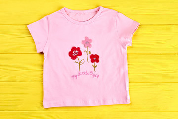 Wall Mural - Baby-girl pink cartoon t-shirt. Toddler girl cotton t-shirt with cartoon flowers, yellow wooden background. Childs new summer clothes.