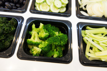 Close up broccoli on salad bar with various fresh vegetables and other foods.