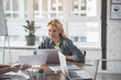 © Yakobchuk Olena - Portrait of blonde serene girl sitting in front of computer in office. Her look is chained to document