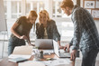 © Yakobchuk Olena - Laughing man and women standing in workplace. They using gadgets for working. Blonde girl staring at camera