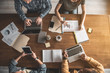 © Yakobchuk Olena - Top view of four people sitting at wooden desk. They using modern technology and writing