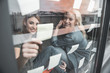 © Yakobchuk Olena - Enjoyed coworkers sitting on windowsill indoors. They are sticking little white papers on window glass with pleasure
