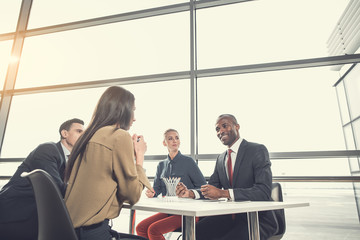 Wall Mural - Low angle cheerful woman speaking with pleased colleagues while sitting at table in contemporary office. Positive partners during job concept