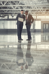 Full length outgoing males looking at notebook computer while standing indoor. Cheerful colleagues during labor concept. Copy space