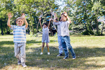 Wall Mural - adorable little children catching soap bubbles while spending warm summer day in public park illumin