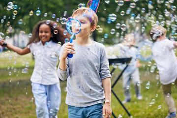 Wall Mural - multi-ethnic group of little kids having fun at green public park while making colorful soap bubbles