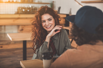 Portrait of joyful young woman flirting with man in cafe. She is looking at boyfriend playfully and smiling