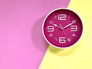 Wall Mural - Closeup A deep pink wall clock set on pastel pink and yellow background. Theme of Working business time .The concept of 