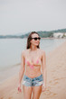 © LIGHTFIELD STUDIOS - smiling girl in sunglasses and bikini top looking away on ocean beach