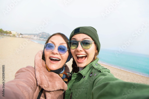 Photographie Mother and adult daughter are doing selfie on the beach going crazy and showing tongueSunset light