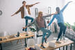 high angle view of happy multiethnic business colleagues dancing on tables in modern office