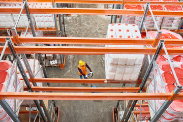 Wall Mural - Top view background image of tall shelf rows in modern warehouse with worker wearing hardhat pulling empty moving cart in aisle, copy space