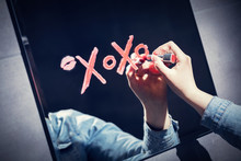 Woman Writing Xoxo On A Mirror With Red Lipstick.