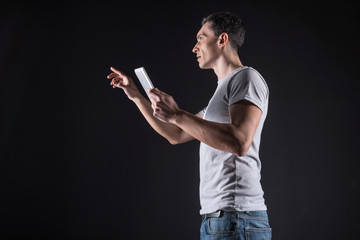 Modern IT technology. Serious handsome nice man holding a tablet and looking at the digital screen while working as a programmer