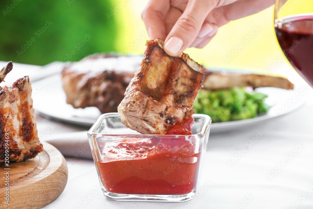 Woman dipping ribs into ketchup on table