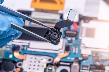 The asian technician pull a camera out of the tablet's motherboard for repairing in the lab. the concept of computer hardware, mobile phone, electronic, repairing, upgrade and technology.