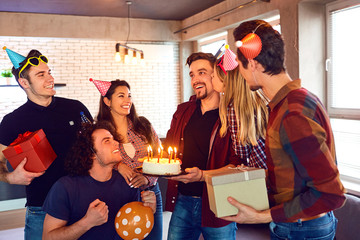 Friends with cake with candles celebrating birthday at a party in room.