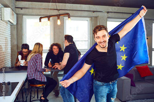 Foto Young man with the european flag in his hands on the background of friends in the room