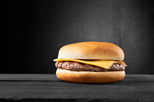 Plain Beef Burger With Cheese On Wooden Table Isolated On Black Background.