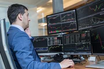 Wall Mural - Male stock broker trading online watching charts and data analyses on multiple computer screens.