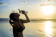 thirsty beautiful Asian sport runner woman drinking water in front of the sea after running workout tired and dehydrated at sunset orange sky beach