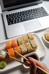 Wall Mural - Food delivery service. Sushi rolls assortment fresh from a restaurant. Laptop online meal order