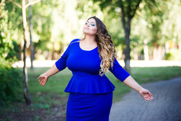 Plus size fashion model in blue dress outdoors, beauty woman with professional makeup and hairstyle, freedom concept