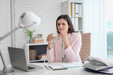 Canvas Print - Young woman taking pill against headaches while sitting at table in office