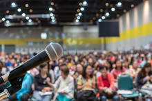 Microphone Over The Abstract Blurred Photo Of Conference Hall Or Seminar Room In Exhibition Center Background With Speakers On The Stage And Attendee Background, Business Meeting And Education Concept